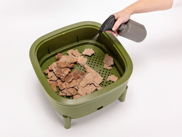 Brauner Karton in einer grünen Wurmbox Befeuchten von braunen Kartonresten in einer grünen Wurmbox